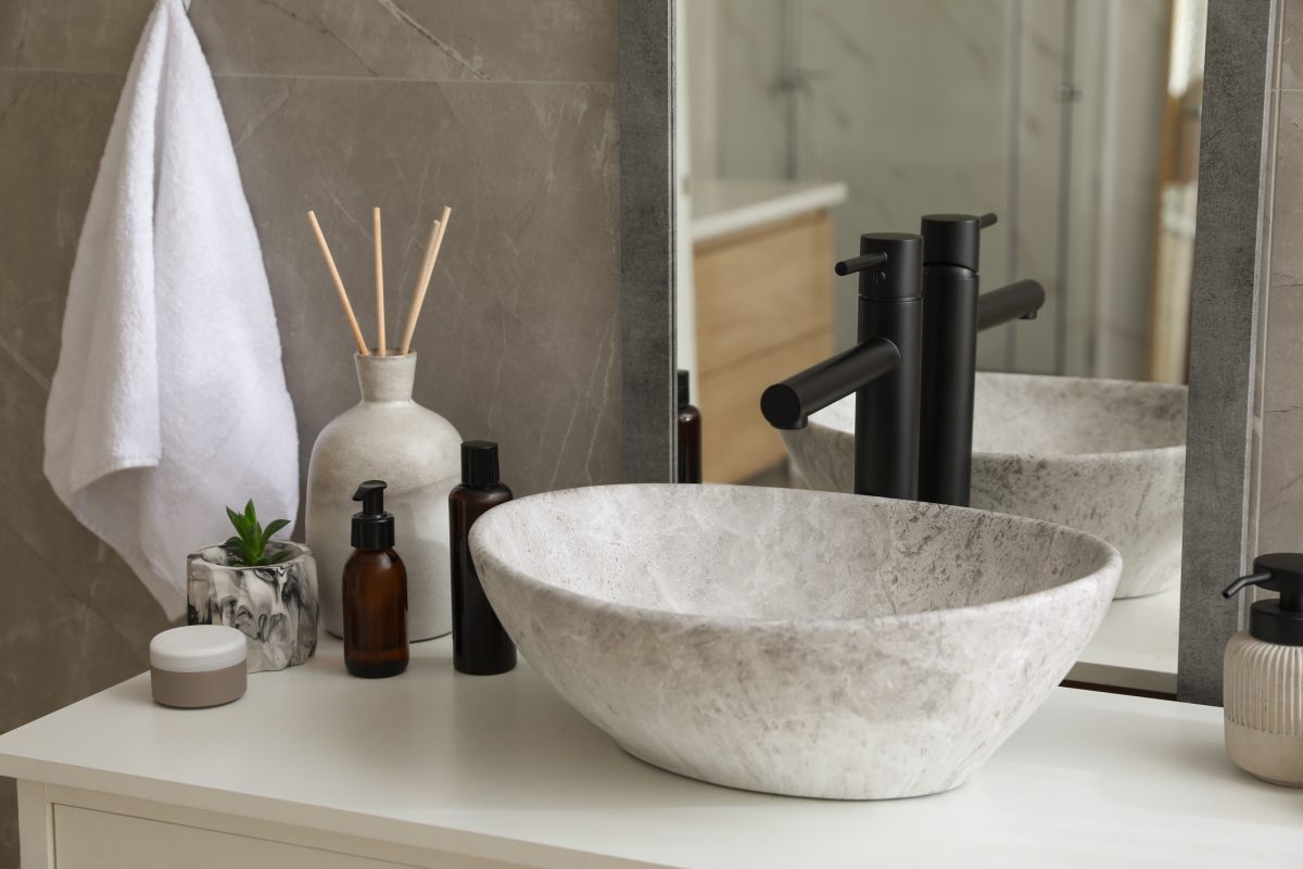Stone vessel sink with faucet and toiletries on white countertop in bathroom